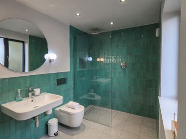A bathroom with a wall-mounted sink toilet and walk-in shower with green tiles at Gillside in Millbeck