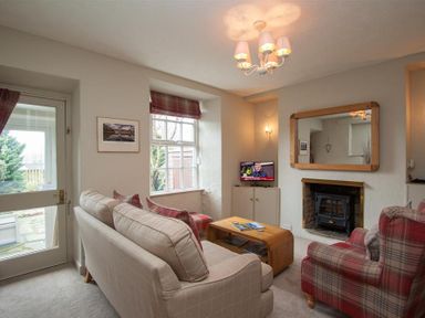 A living room with a beige sofa, a red plaid armchair, a wooden coffee table, a TV on a cabinet, and a fireplace at Swallow's Nest in Windermere