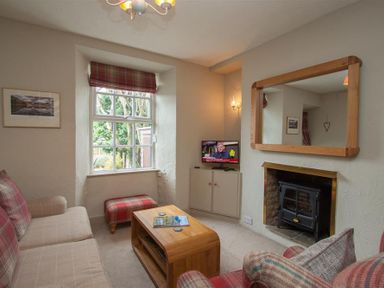 A living room with a sofa armchair wooden coffee table and a television above a cabinet by a window at Swallow's Nest Windermere
