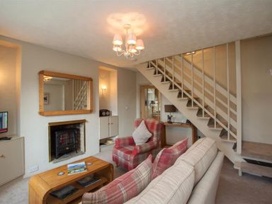 A living room with a plaid armchair a sofa a wooden coffee table a fireplace and stairs at Swallow's Nest in Windermere