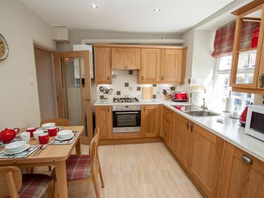 A kitchen with wooden cabinets a dining table set for four and window at Swallow's Nest in Windermere
