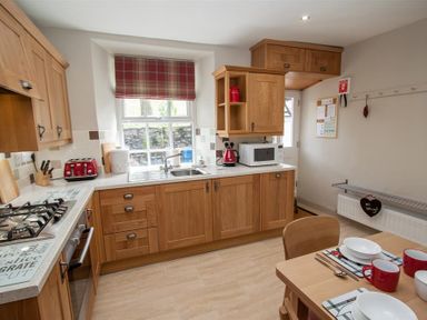 A kitchen with wooden cabinets a dining table set with bowls and mugs at Swallow's Nest in Windermere