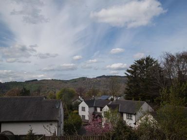 Several houses surrounded by trees with hills in the background under a cloudy sky at Swallow's Nest in Windermere