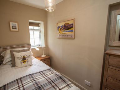 A bedroom with a single bed a bedside table with a lamp framed pictures on the walls and a wooden dresser at Swallow's Nest in Windermere