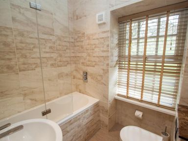 A bathroom with a bathtub a sink a toilet and a window with blinds at Swallow's Nest in Windermere