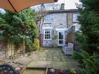 A stone patio with a bench tree and plants outside a stone house at Swallow's Nest in Windermere