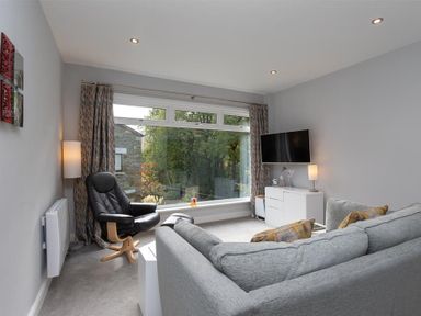 A living room with a large window black chair gray sofa TV on wall and white cabinet at Silver Howe in Grasmere