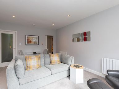 A sitting room with a grey sofa with yellow plaid cushions and a small white side table at Silver Howe in Grasmere