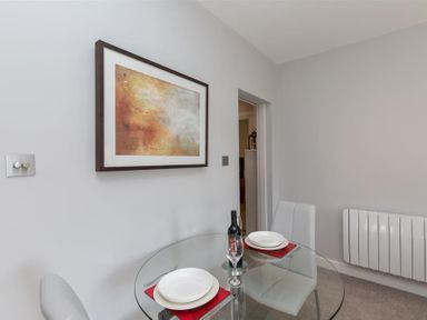 A dining area with a round glass table set for two white chairs and abstract wall art at Silver Howe in Grasmere
