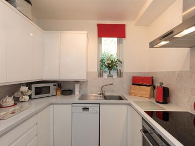 A kitchen with white cabinets a microwave flowers on a window ledge and red kitchen appliances at Silver Howe in Grasmere