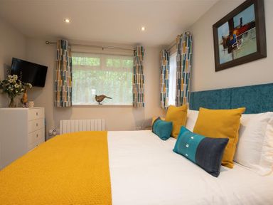 A bedroom with a bed featuring yellow and teal pillows and a yellow blanket beside a window with patterned curtains at Silver Howe in Grasmere