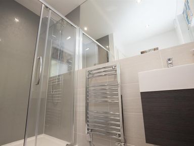 A bathroom with a glass shower enclosure a chrome towel radiator and a sink with a dark cabinet at Silver Howe in Grasmere