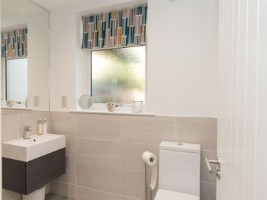 A bathroom with a sink, toilet, window with patterned blind, and mirror at Silver Howe in Grasmere