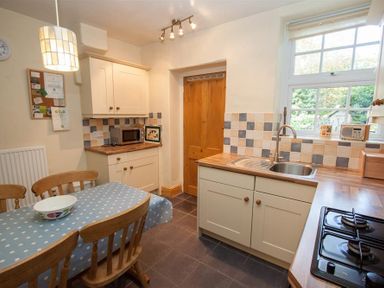 A kitchen with wooden chairs around a table covered with a blue polka dot tablecloth at Briardale Cottage in Ambleside