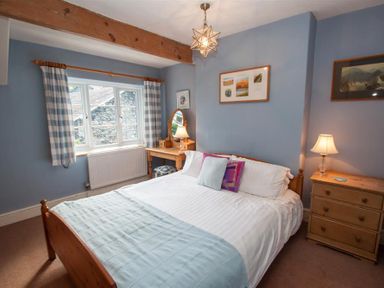 A bedroom with a wooden bed chest of drawers a dressing table and blue checked curtains at Briardale Cottage in Ambleside