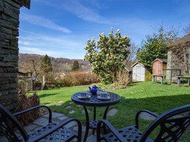 A garden with a small round table set with a teapot and cups and metal chairs on a stone patio at Briardale Cottage in Ambleside
