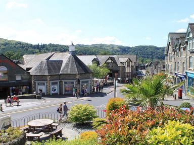A town street with stone buildings people walking and sitting and plants in the foreground at Briardale Cottage Ambleside