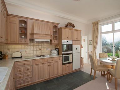 A kitchen with wooden cabinets a stove a refrigerator and a dining table with chairs by a window at Betamere in Ambleside