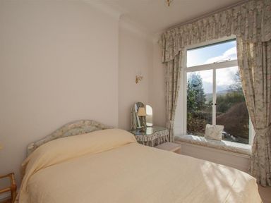 A bedroom with a bed a dressing table and a window seat with floral curtains at Betamere in Ambleside