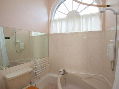 A bathroom with a bathtub shower toilet and a large arched window at Betamere in Ambleside