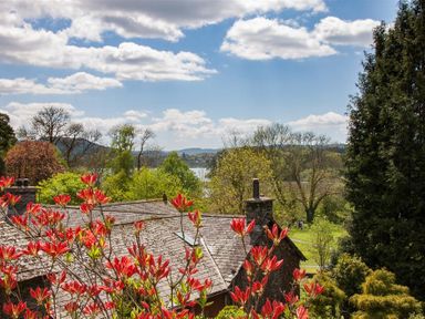 View of a rooftop with chimney surrounded by trees with red leaves and hills in the background at Betamere in Ambleside