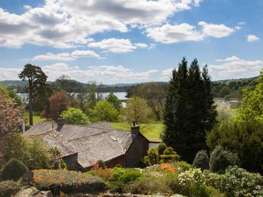 A garden with trees and bushes overlooking a stone house and a lake in the distance at Betamere in Ambleside