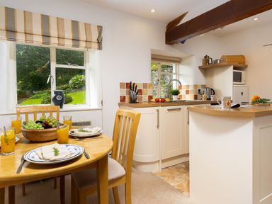 A kitchen and dining area with wooden table set with plates and orange juice and a kitchen counter with sink and appliances at The Hayloft in Ambleside