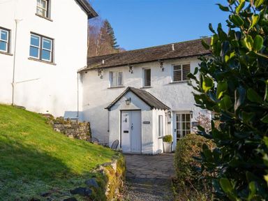 Exterior of a white cottage with stone pathway and garden greenery at The Hayloft in Ambleside