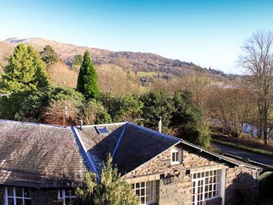 A stone house with a tiled roof and trees on a hillside at The Hayloft in Ambleside