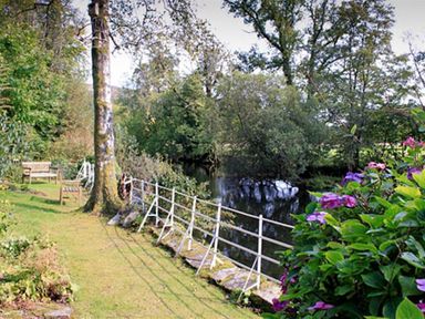 A garden with benches and a metal railing next to a river surrounded by trees and flowers at The Hayloft in Ambleside