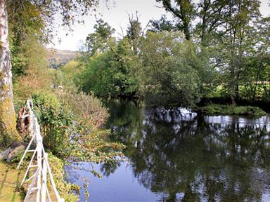 A river surrounded by trees and bushes with a white fence along the riverbank at The Hayloft in Ambleside