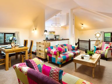 A living room with colorful patchwork sofas a wooden coffee table and a dining table at Falls View Cottage in Ambleside