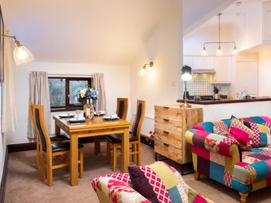 A dining area with a wooden table and chairs next to a sitting area with patchwork upholstered sofas at Falls View Cottage in Ambleside
