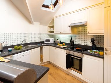 A kitchen with white cabinets black countertops and kitchen appliances at Falls View Cottage in Ambleside