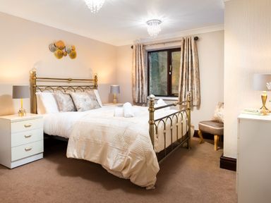 A bedroom with a brass bed frame two bedside tables with lamps a window with curtains and a chair at Falls View Cottage in Ambleside