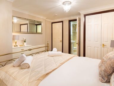 A bedroom with a bed and rolled towels on it a dresser with a lamp and plant a mirror and doors including one leading to a bathroom at Falls View Cottage in Ambleside