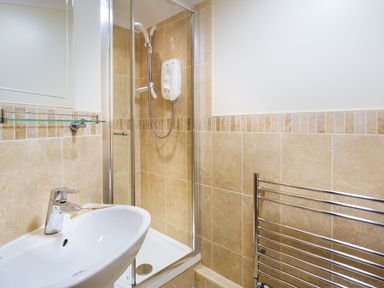 A bathroom with a white sink a glass shelf a shower with a handheld showerhead and a metal towel rack at Falls View Cottage in Ambleside