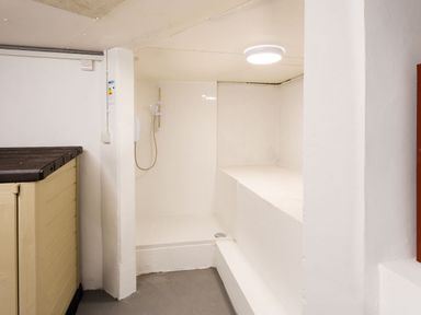 A small shower area with a hand shower and a large beige plastic storage container in a white room at Falls View Cottage in Ambleside