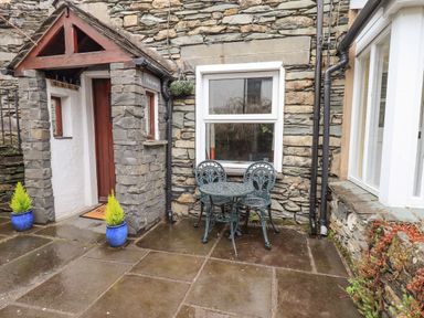 A stone exterior wall with a wooden door under a small roof and a metal table with two chairs outside at Hideaway Cottage in Ambleside