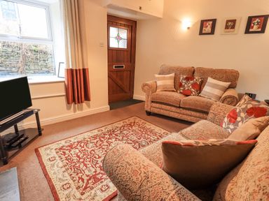 A living room with two sofas a patterned rug a wooden door and a television at Hideaway Cottage in Ambleside