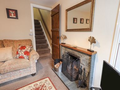 A living room with a patterned sofa cushions a stone fireplace with a firewood holder stairway and a mirror at Hideaway Cottage Ambleside
