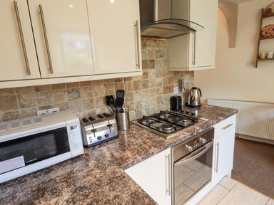 A kitchen countertop with a microwave, toaster, utensils, gas stove, kettle and cabinets at Hideaway Cottage in Ambleside