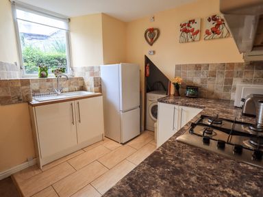 A kitchen with a sink under a window a white fridge a washing machine in a corner and a gas stove on a counter at Hideaway Cottage in Ambleside