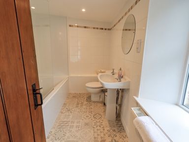 A bathroom with a bathtub shower sink toilet round mirror and patterned tile floor at Hideaway Cottage in Ambleside