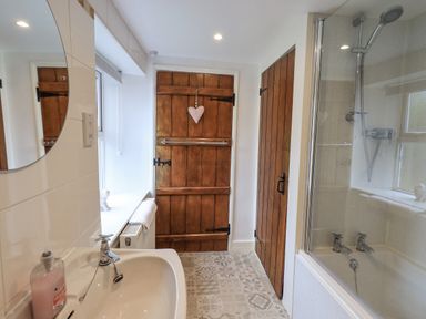 A bathroom with a sink mirror wooden doors bathtub with shower at Hideaway Cottage in Ambleside