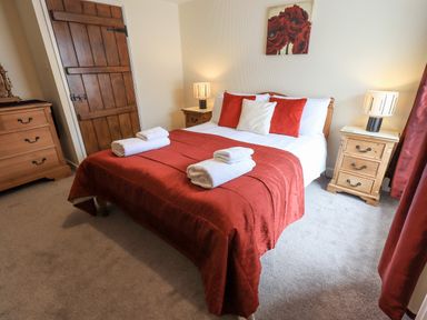 A bedroom with a bed covered in a red bedspread and white towels on top with wooden furniture at Hideaway Cottage in Ambleside