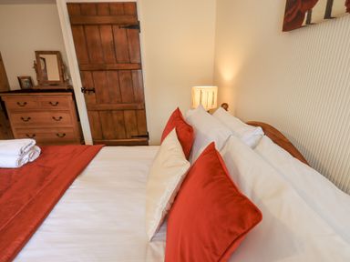 A bedroom with a bed with red and white pillows a wooden door a wooden dresser a lamp and folded towels on the bed at Hideaway Cottage Ambleside