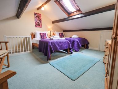 A bedroom with two single beds covered in purple bedspreads and a skylight window at Hideaway Cottage in Ambleside