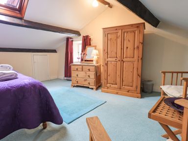 A bedroom with wooden wardrobe chest of drawers and chair with purple bedspread at Hideaway Cottage in Ambleside