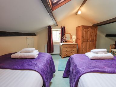 A bedroom with two single beds covered with purple bedspreads and white towels on them at Hideaway Cottage in Ambleside